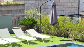 Una piscina de diseño moderno, rodeada por un pequeño césped y algunas sillas de descanso.