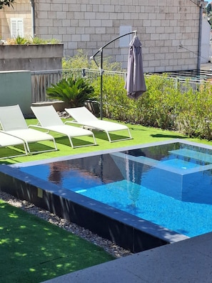 A swimming pool with a modern design, surrounded by a small grassy area and a few lounge chairs.