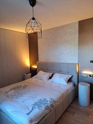 Una camera da letto moderna con un letto grande, una lampada a sospensione geometrica, lampade da comodino e un tavolino.