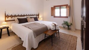 Un dormitorio con cama, mesita de noche, lámpara y ventana con cortinas.