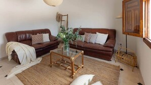 Una sala de estar con dos sofás de cuero marrón, una mesa de centro de vidrio, un tapete tejido y una lámpara colgante.