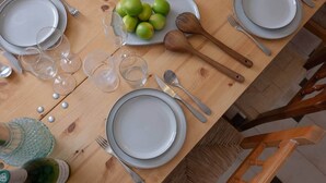 Una mesa de comedor dispuesta con platos, vasos, cubiertos y una botella de vino.