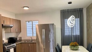 A modern kitchen with stainless steel appliances, a dining area with a marble table, and a view of the outdoors through a window.