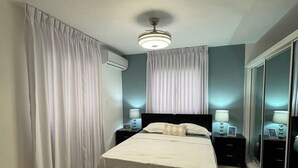 A bedroom with a bed, two bedside tables, a ceiling fan, and a large mirror.