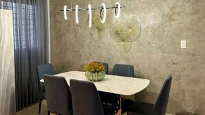 A dining area with a marble table, four chairs, a vase of flowers, and a wall-mounted fan.