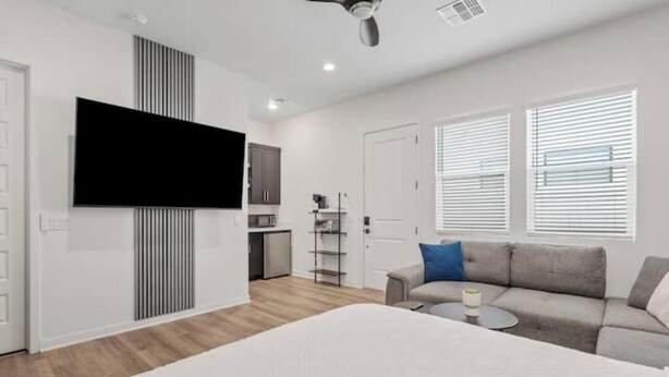 Una sala de estar moderna con una cama grande, un sofá gris, una mesita de centro pequeña y un televisor montado en la pared.