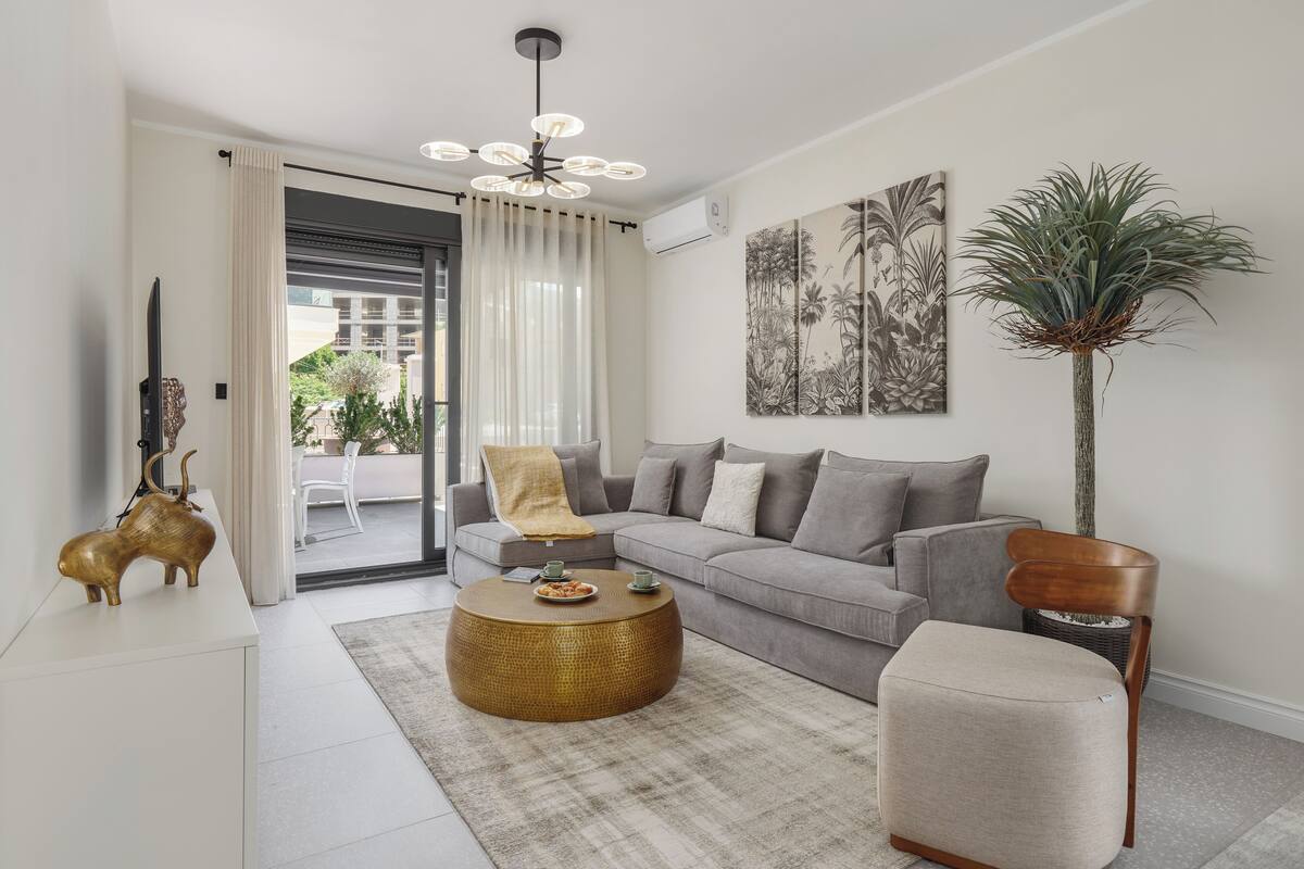 A modern living room with a grey sofa, a round gold coffee table, and a tall plant.