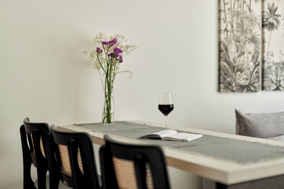 A dining table with chairs, a glass of red wine, and a vase with flowers.