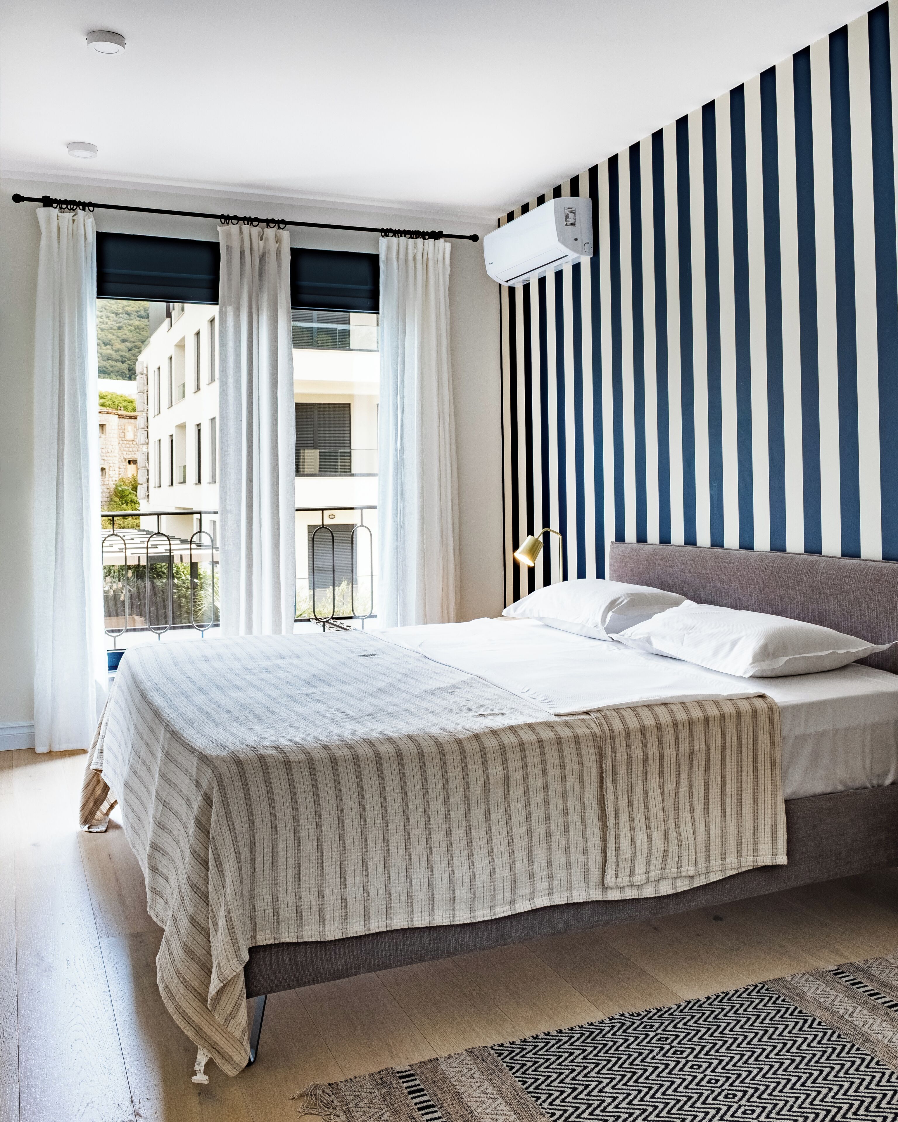 Une chambre à coucher avec un lit, des rideaux, une fenêtre, un climatiseur fixé au mur et un tapis à motifs.