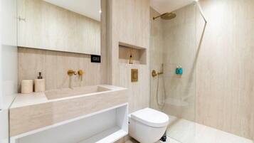 Un baño moderno con un tocador grande, inodoro y zona de ducha con mampara de vidrio.