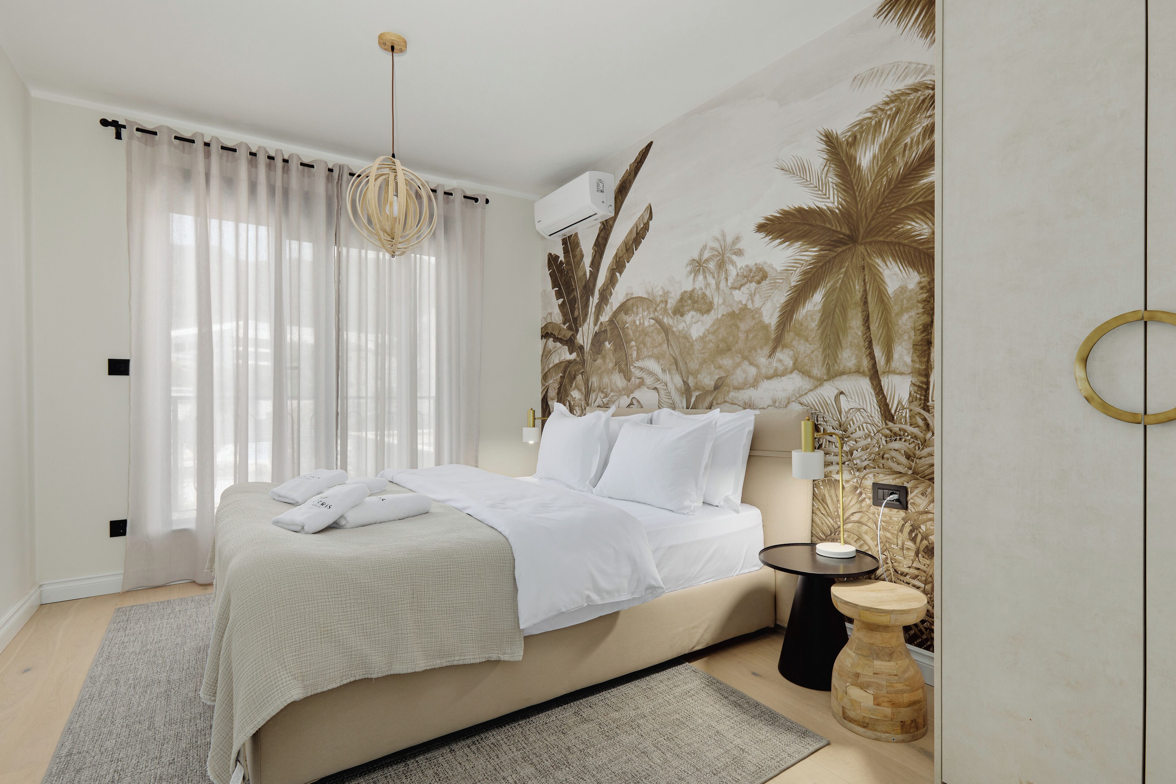 Une chambre à coucher comprenant un lit, une table de chevet, un climatiseur fixé au mur et une fenêtre avec des rideaux légers.