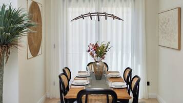 A dining room with a wooden table set for six, surrounded by black chairs. A large vase with flowers is placed in the center.