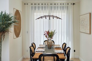 A dining room with a wooden table set for six, surrounded by black chairs. A large vase with flowers is placed in the center.