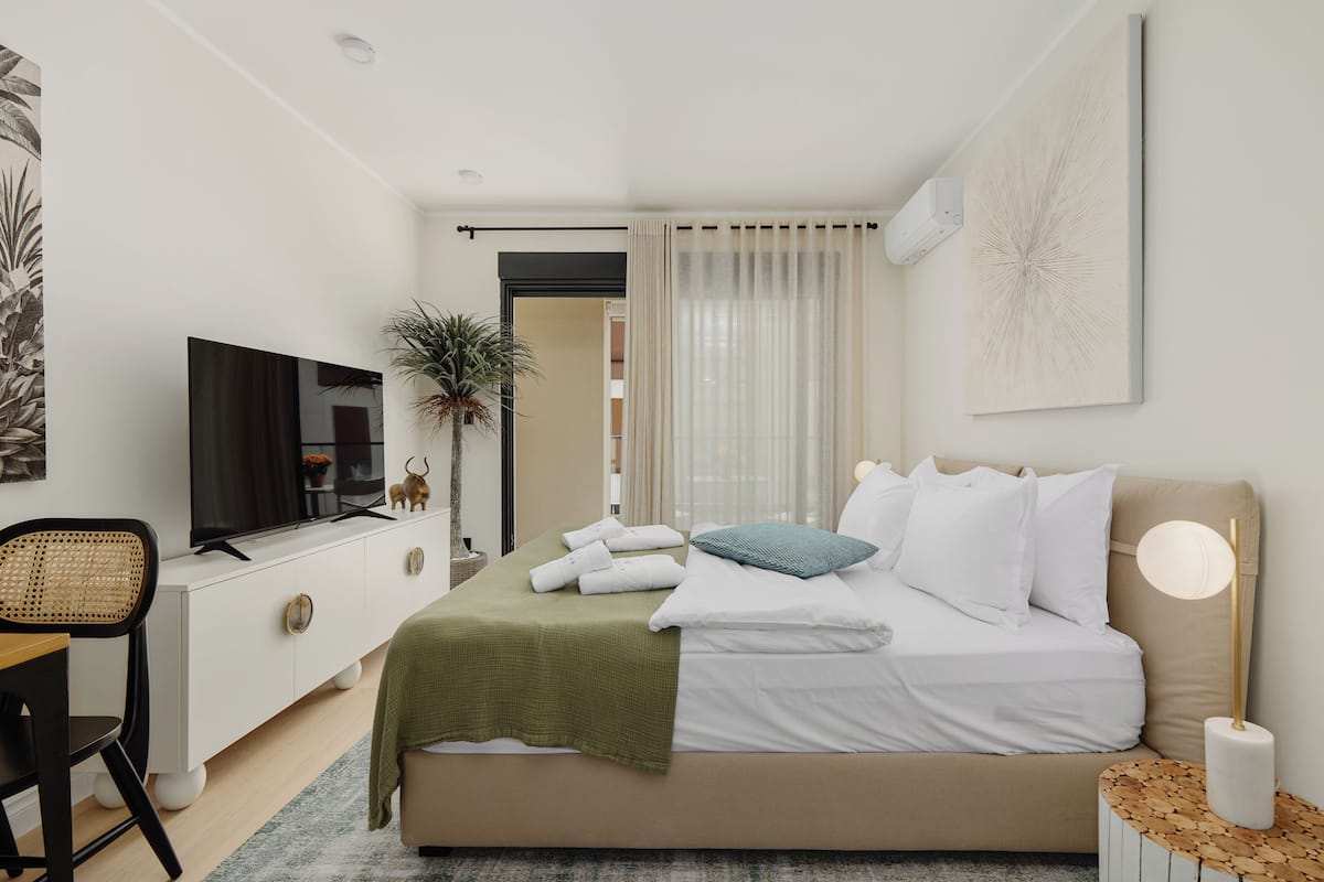 A modern bedroom with a bed, bedside table, TV, and a view of the outside.
