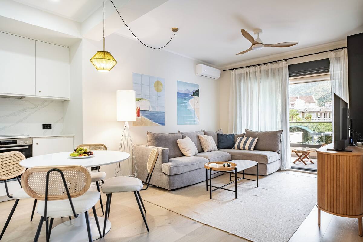 A modern living room with a sofa, dining table, and chairs, a ceiling fan, and artwork on the walls.