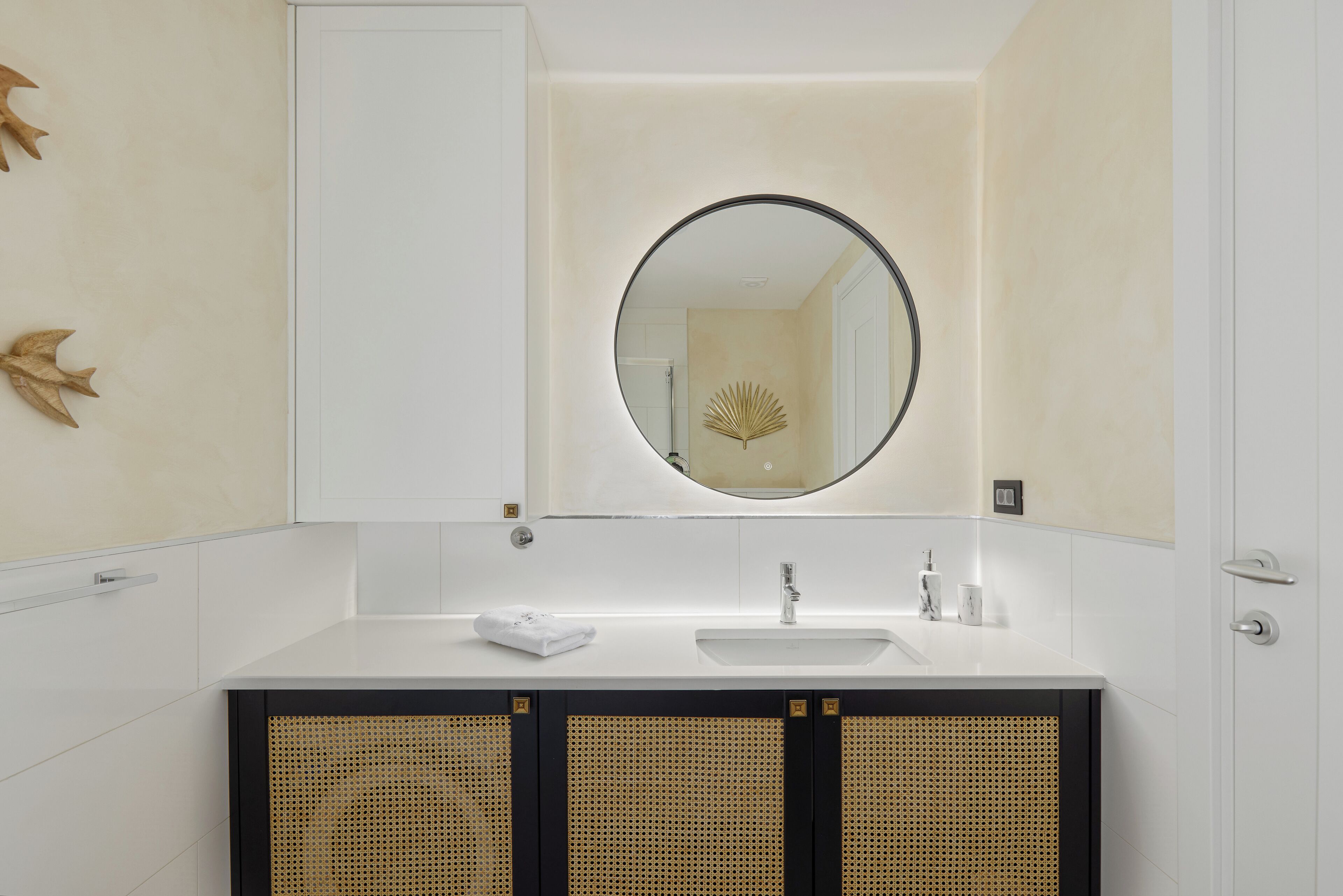 Un baño con tocador blanco, un espejo redondo y un lavabo.