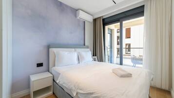 A modern hotel room with a large bed, a bedside table, and a view of the outside balcony.