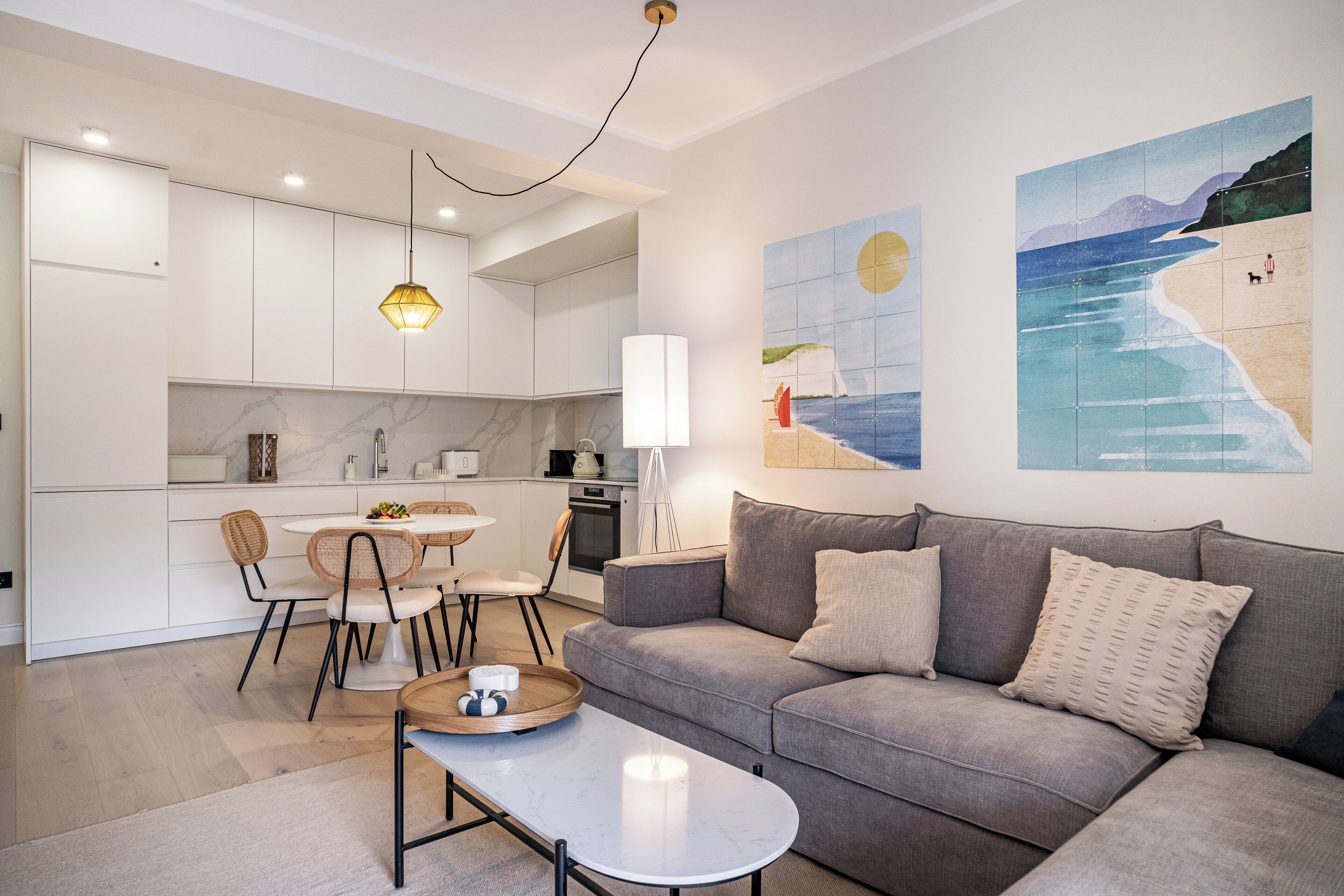 A modern living room with a grey sofa, a coffee table, and a dining area with a white table and chairs.