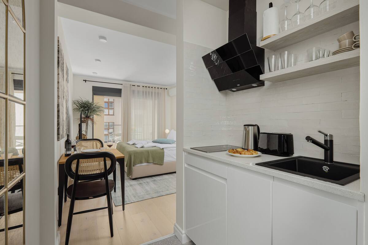 A modern kitchen with white cabinetry, a black range hood, and a countertop with a sink.