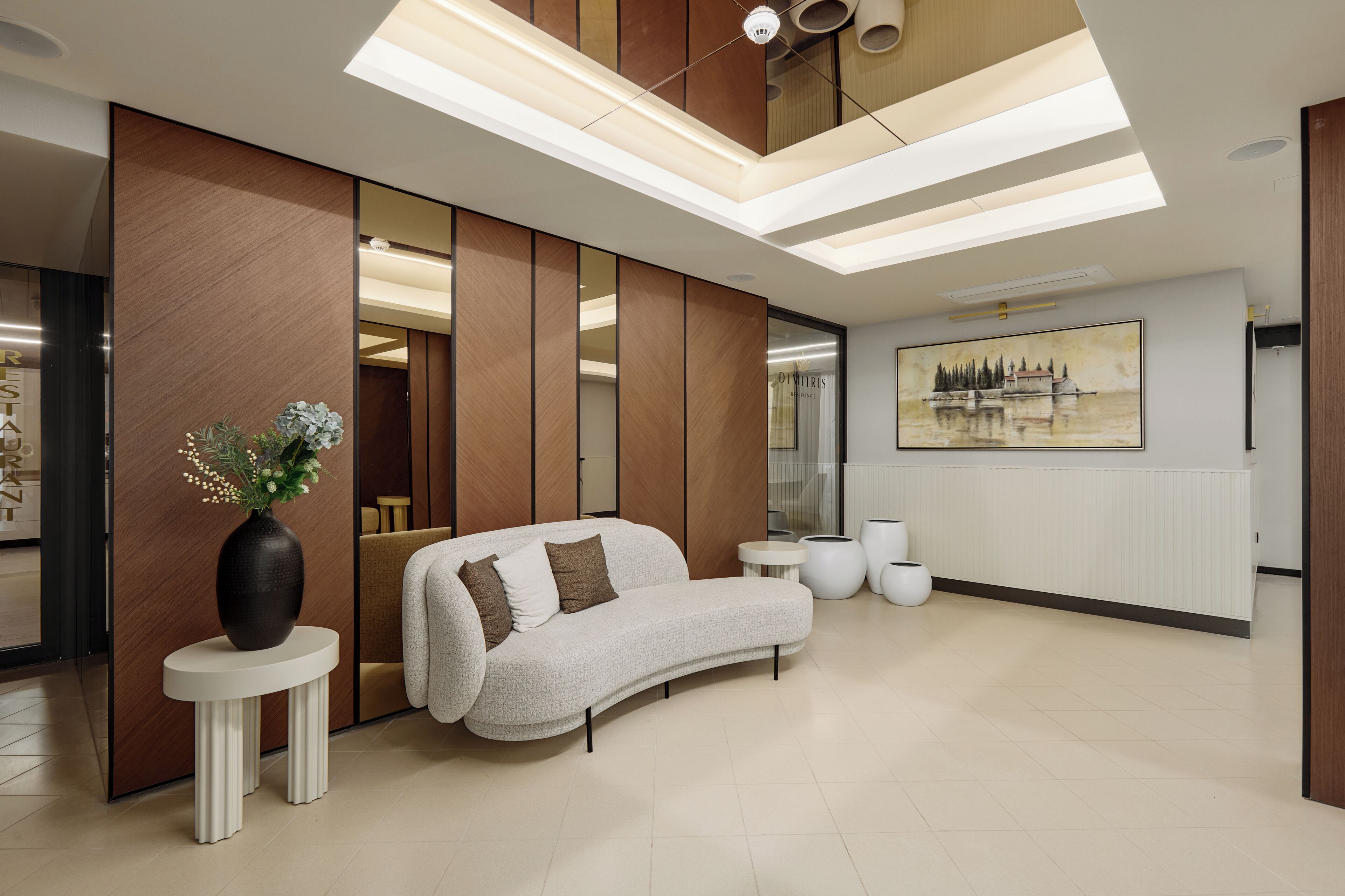 A modern lobby with a curved sofa, a vase with flowers, and a painting on the wall.