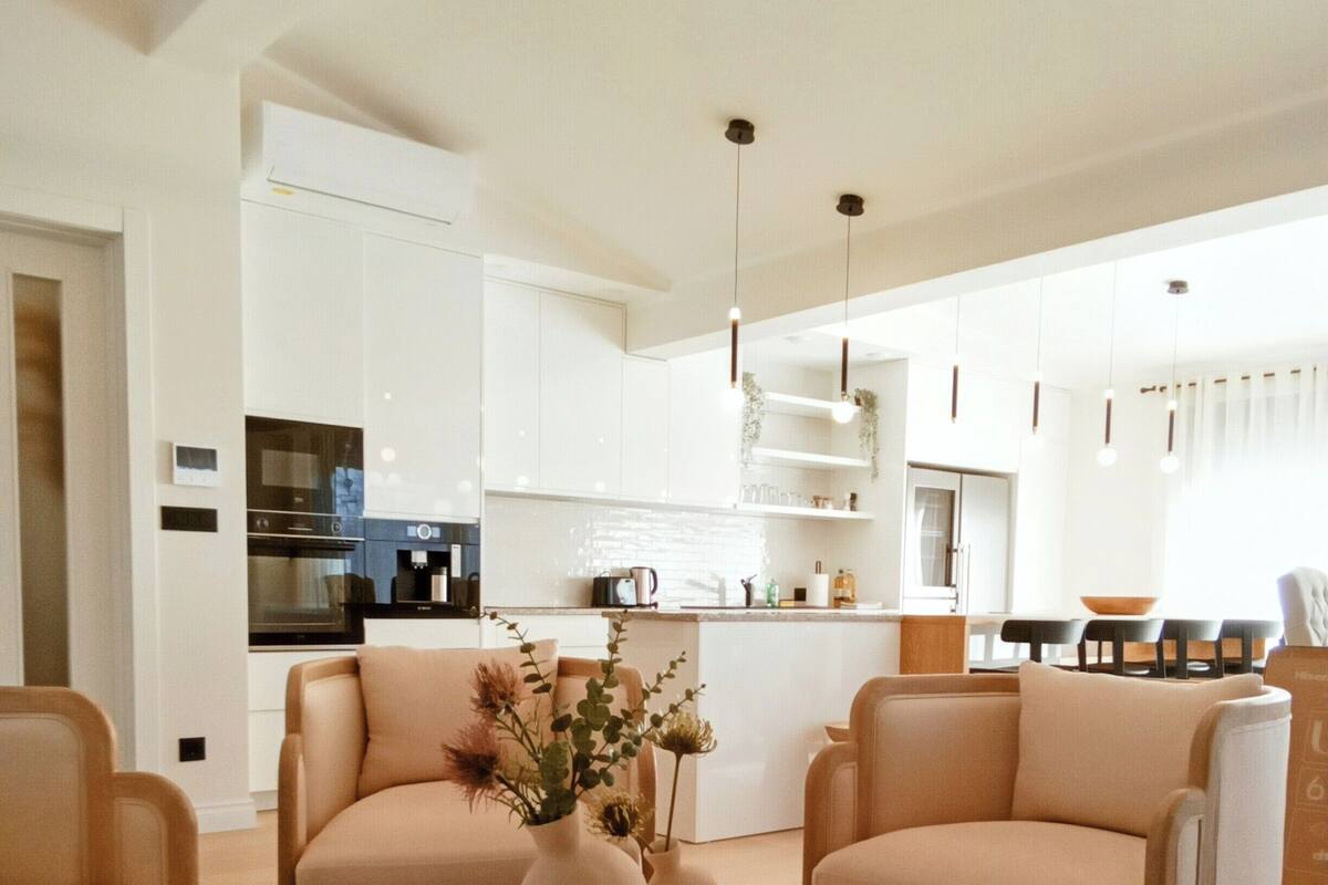 A modern living room with a round glass coffee table, two beige sofas, and a small side table with decorative vases.