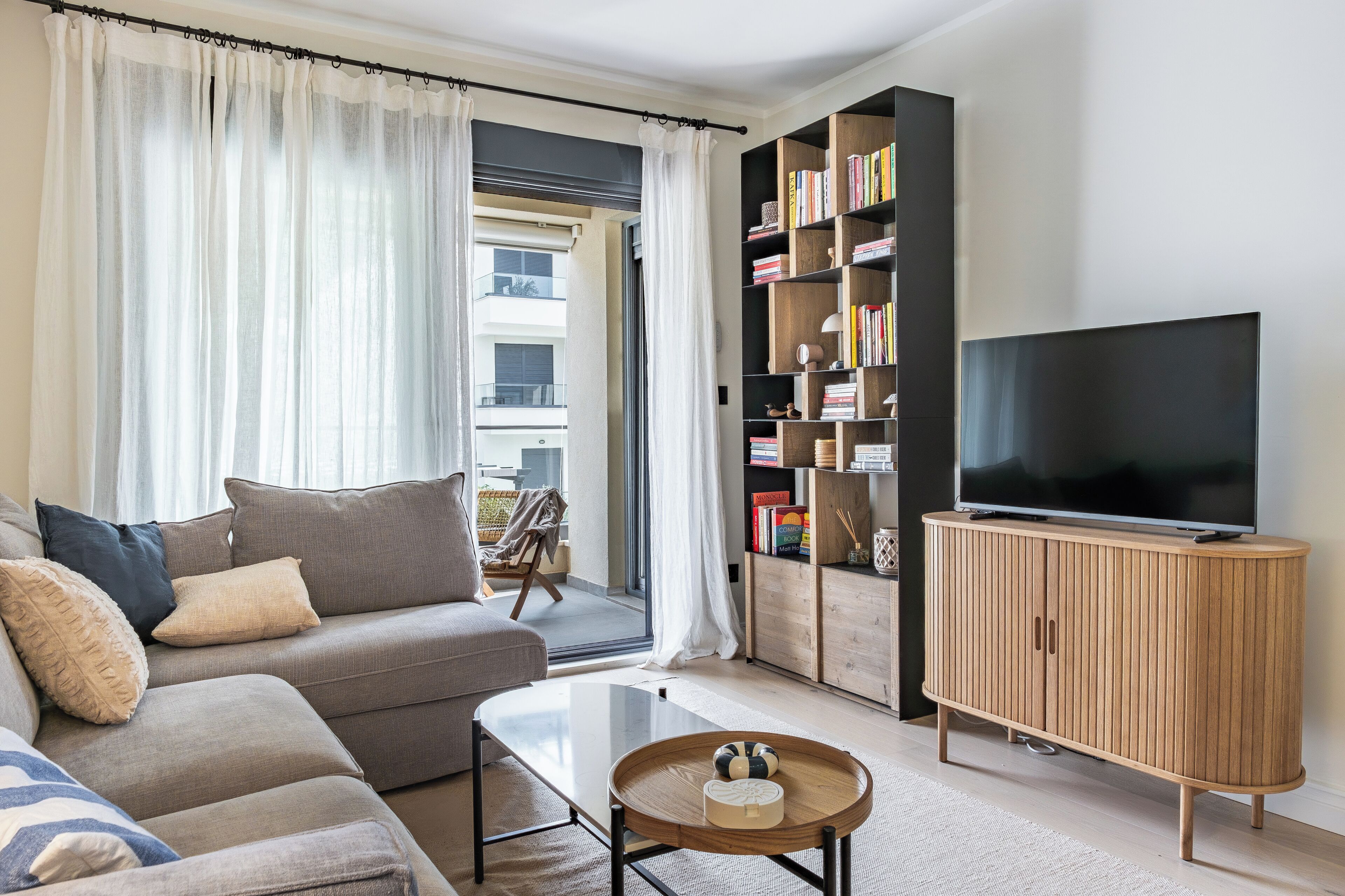 A living room with a sofa, a coffee table, a television, a bookshelf, and a window with curtains.