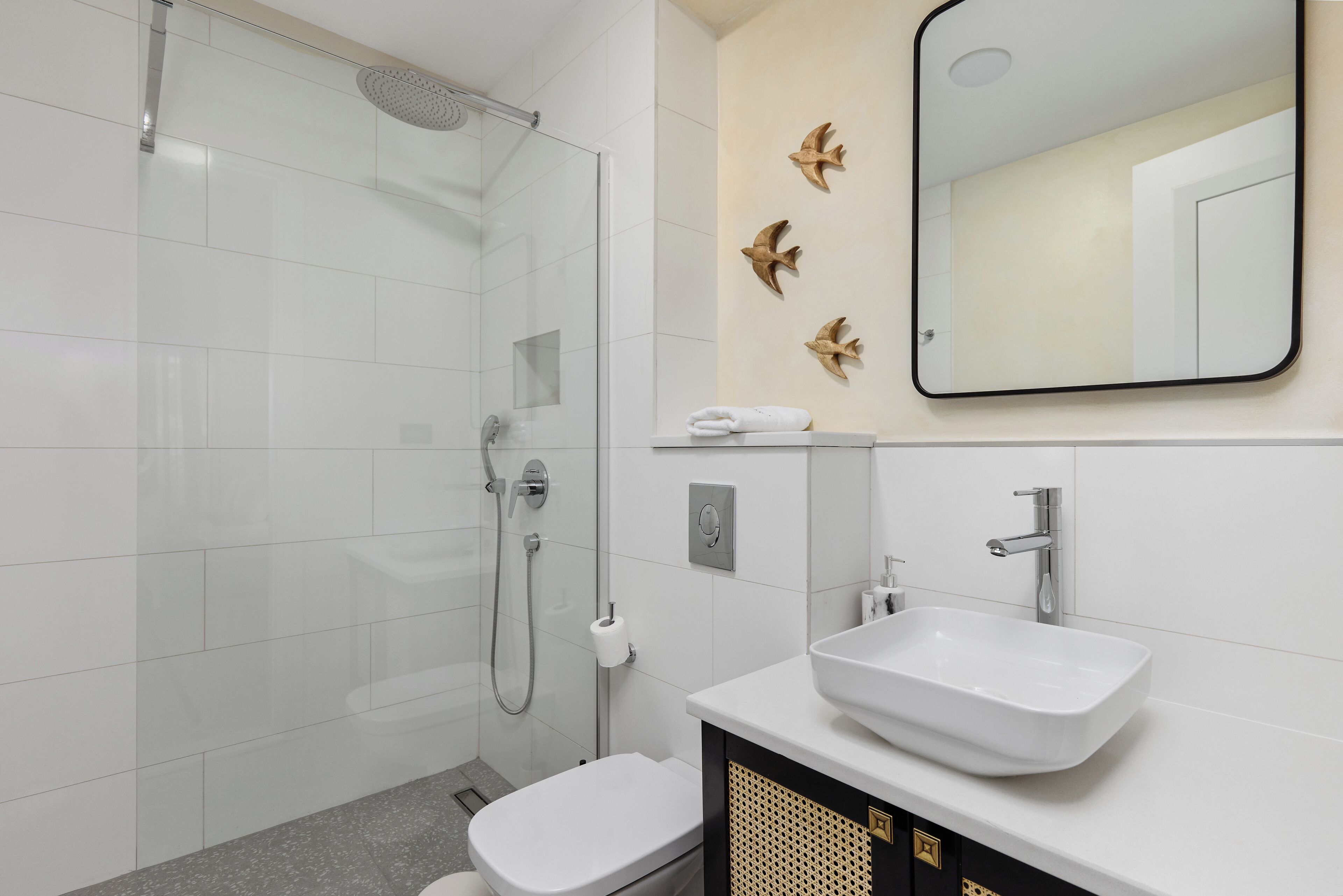 A modern bathroom with a glass shower enclosure, a white toilet, a sink with a vanity, and decorative wall art.