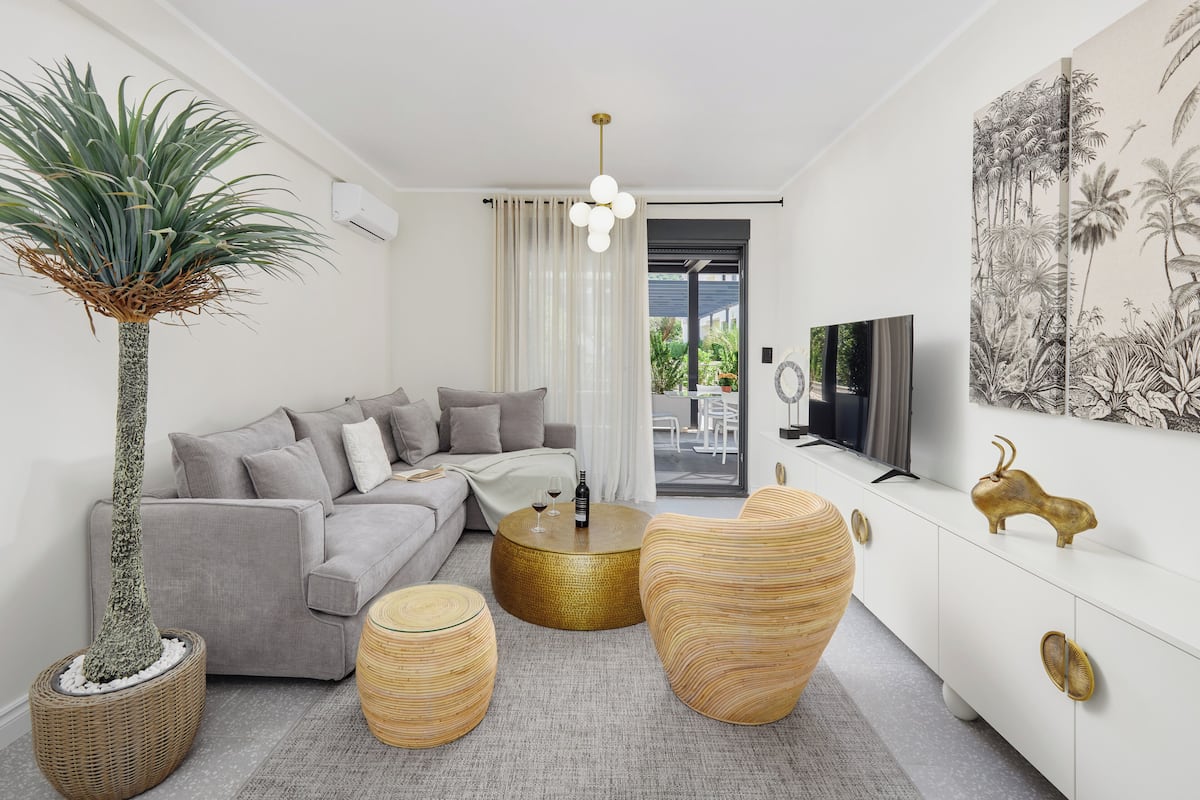A modern living room with a grey sofa, round wooden coffee tables, a large potted plant, and a white cabinet with a television.