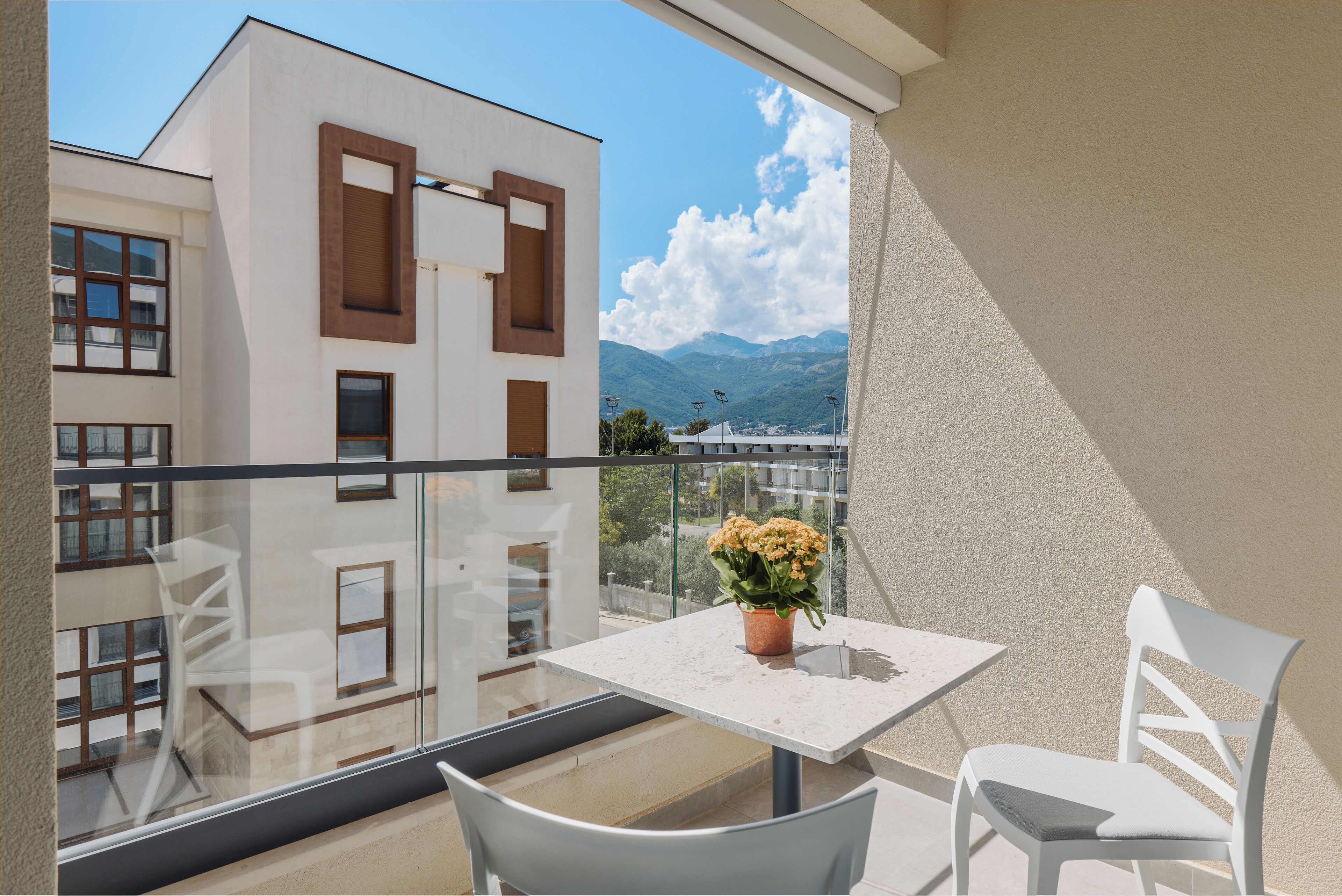 Un balcon avec une table et des chaises, un pot de fleurs et une vue sur des immeubles et des montagnes.