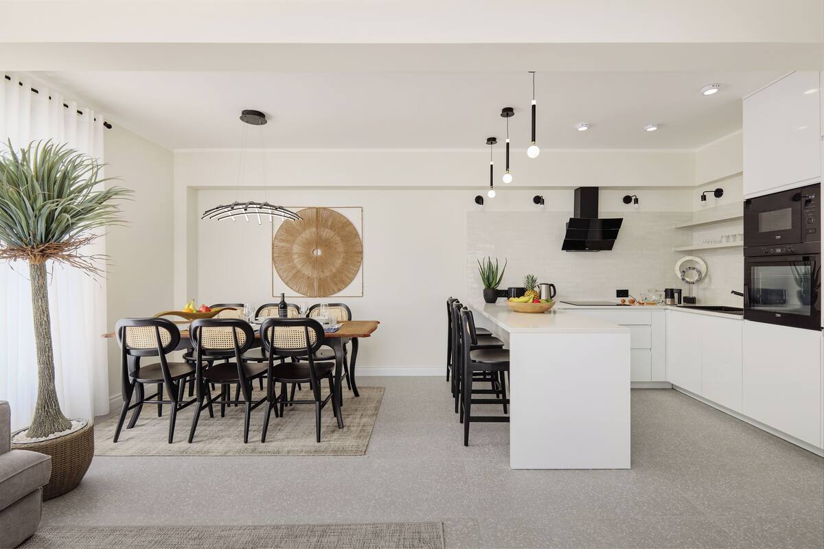 A modern kitchen with white cabinetry, a central island, and a dining area with a round table and chairs.