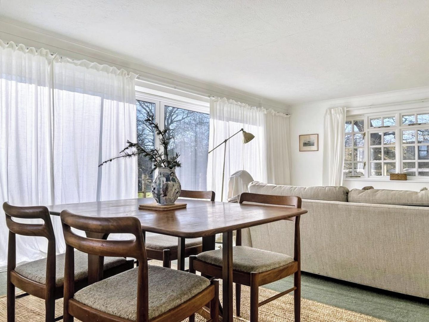 Un coin repas avec une table, des chaises, un vase décoré de branches et un canapé en arrière-plan.