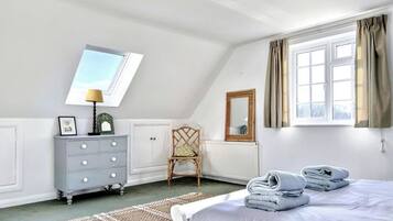 A bedroom with a bed, a dresser, a chair, a window with curtains, and a skylight.
