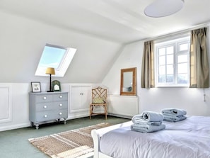Een slaapkamer met een bed, een kaptafel, een stoel, een raam met gordijnen en een dakraam.