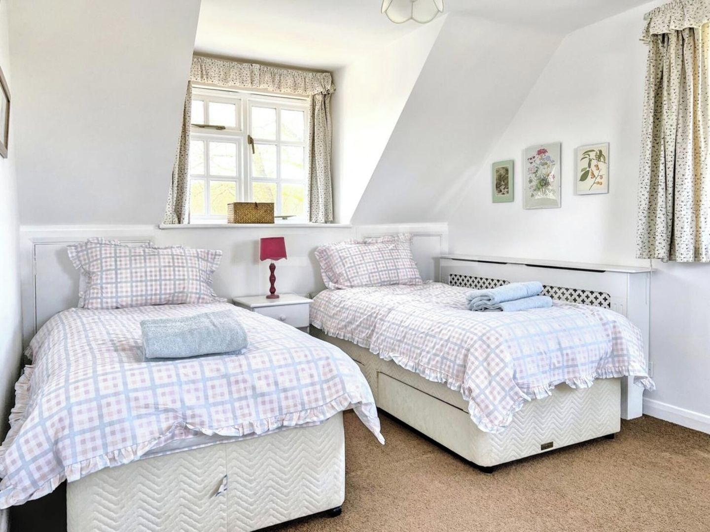 Een slaapkamer met twee bedden, een raam met gordijnen, een nachtkastje met een lamp en wanddecoratie.