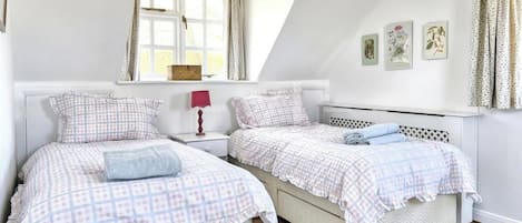 Un dormitorio con dos camas, una ventana con cortinas, una mesita de noche con lámpara y una obra de arte en la pared.