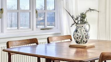 Une table à manger avec quatre chaises, un vase décoratif avec une plante, et une fenêtre donnant sur des arbres et une maison.