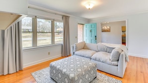 A living room with a grey sofa, patterned ottoman, and a view of a brick wall and a blue door. - 1 Mi to Dwtn Shops & Dining: Spacious Family Home (Hartwell)