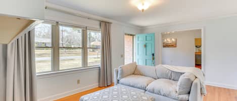 Ein Wohnzimmer mit grauem Sofa, gestreiftem Hocker und Blick auf eine Ziegelwand und eine blaue Tür.