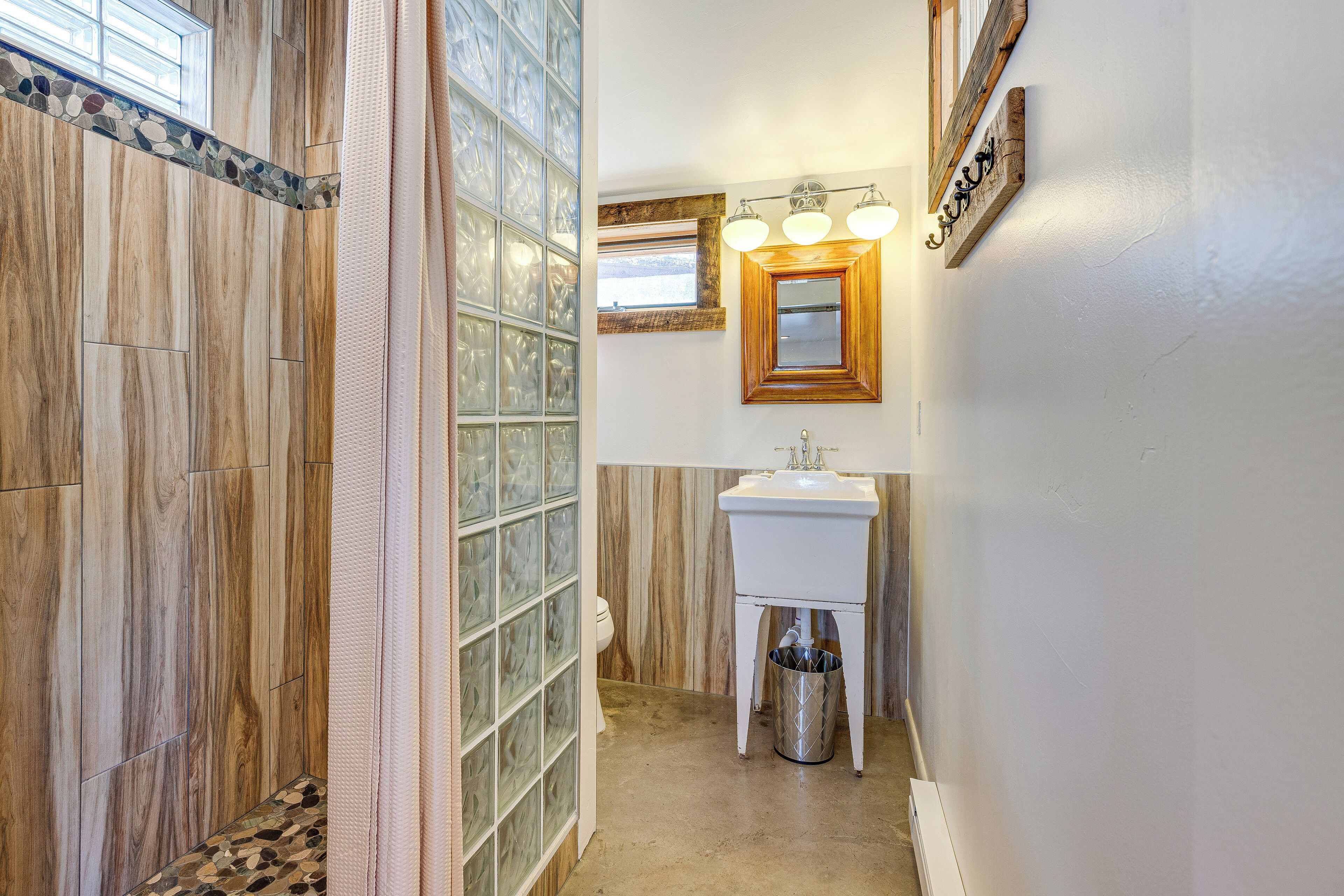 Un baño con suelo de madera, cabina de ducha de vidrio, lavabo blanco y espejo con iluminación.