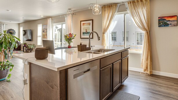 A modern kitchen with a central island, stainless steel appliances, and a large window with curtains. - Beautiful Home w/ Bonus Room & Prime Location! (Brighton)