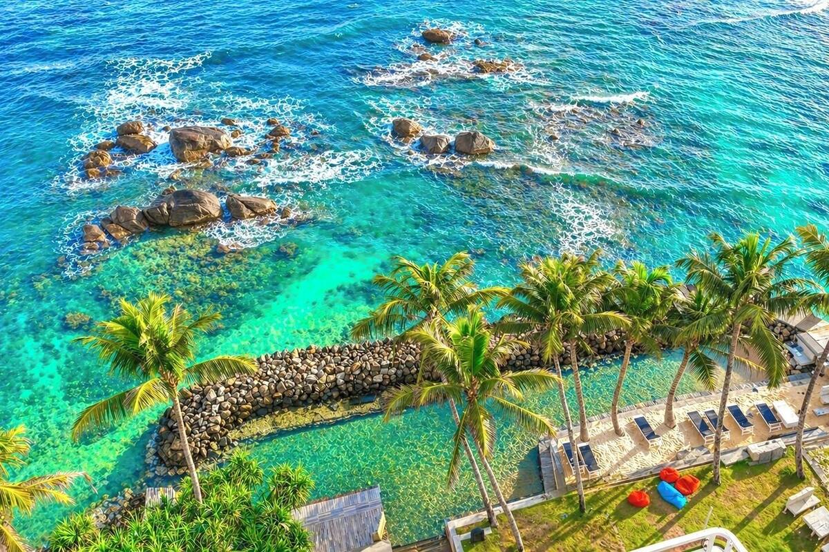 A beach resort with clear turquoise waters, palm trees, and sun loungers.