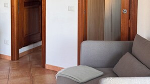 Una habitación con un sofá gris, puertas de madera y suelo de baldosas.