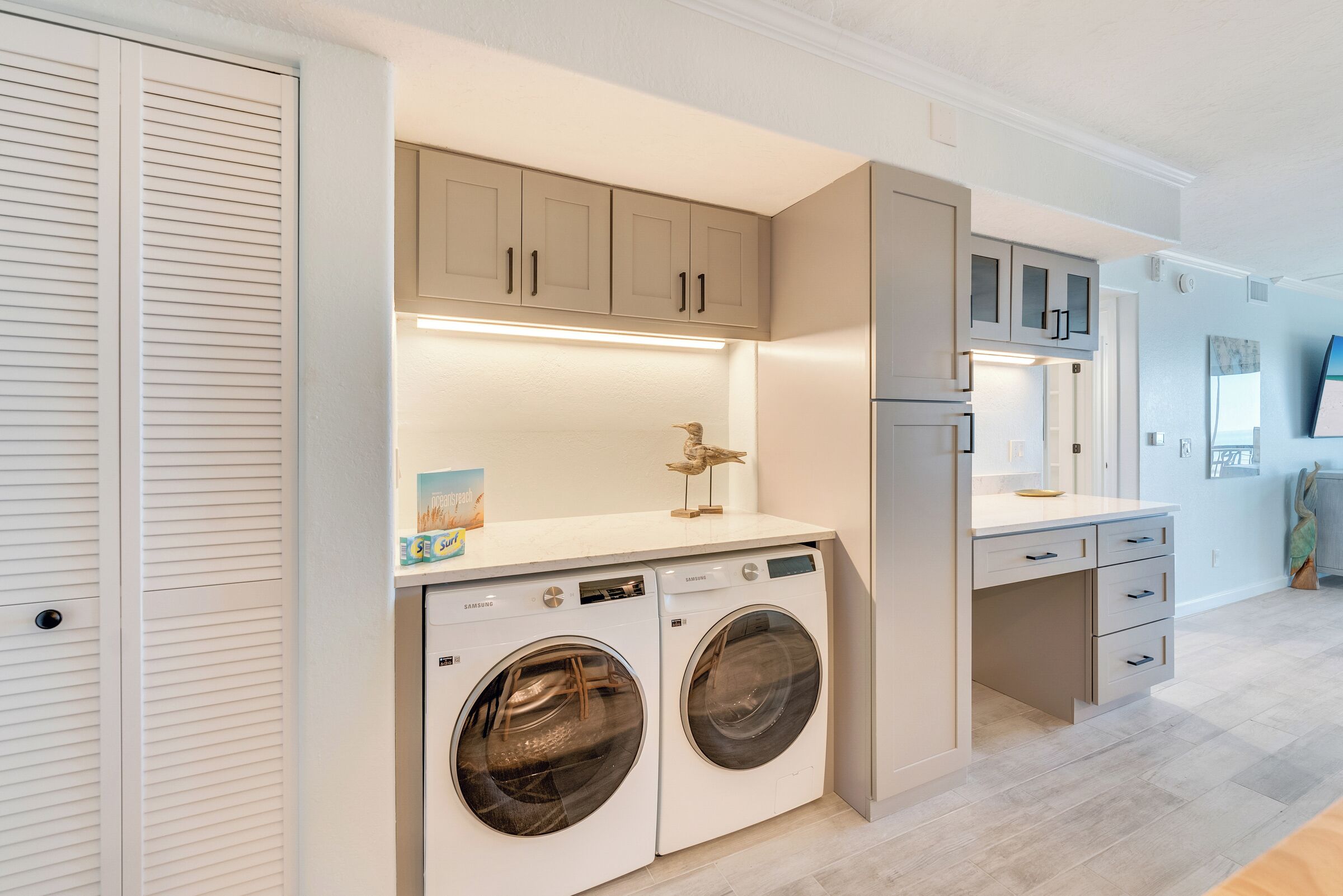A laundry room with two white front-loading washers, a countertop with a bird sculpture, and cabinets above.
