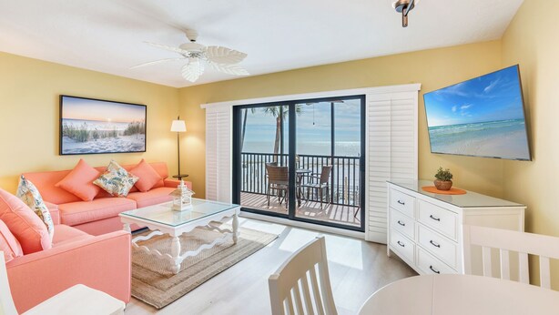A bright living room with a pink sofa, a glass coffee table, and a view of the beach through large sliding doors. - OCEAN'S REACH 2X2: 1-Bdrm, Gulf-Front View, All Amenities Open! (Sanibel Island)