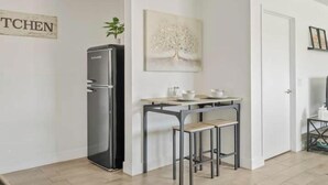 A modern kitchen with a refrigerator, a dining table with stools, and a wall-mounted artwork. - Detached Private Guesthouse - Full Kitchen, 1BD + 1BA, Parking Spot - Sleeps 2 (Mesa)