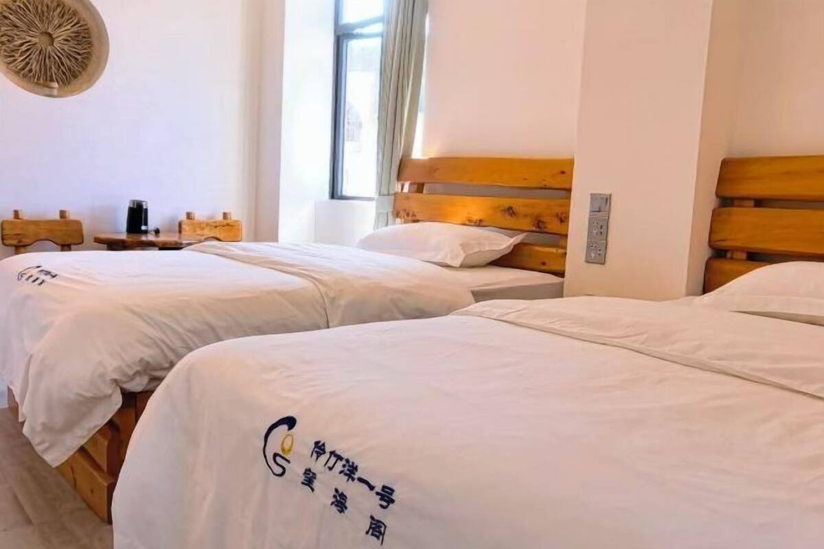 A hotel room with two beds, a wooden headboard, a small table with a coffee maker, and a window with curtains.