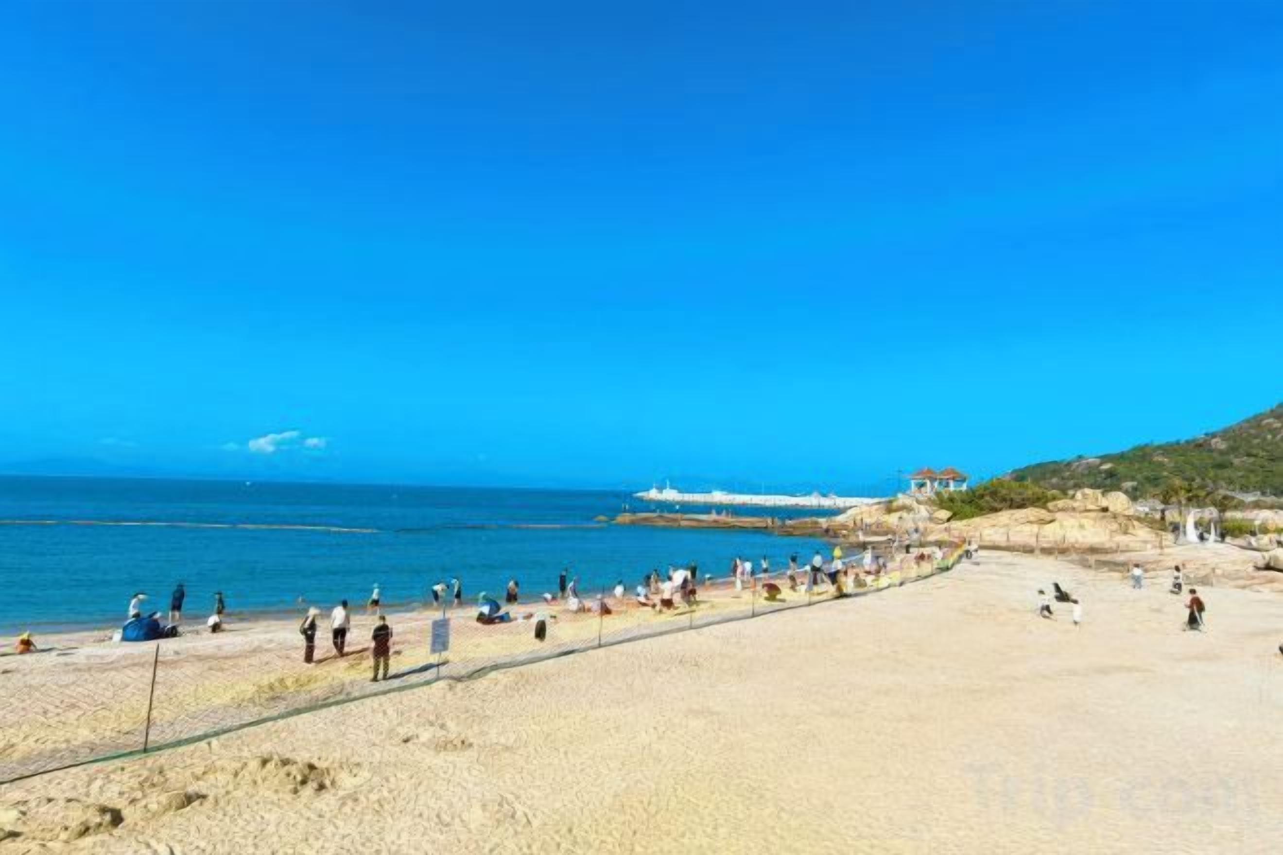 Une plage avec un ciel dégagé, un rivage sablonneux et quelques personnes.