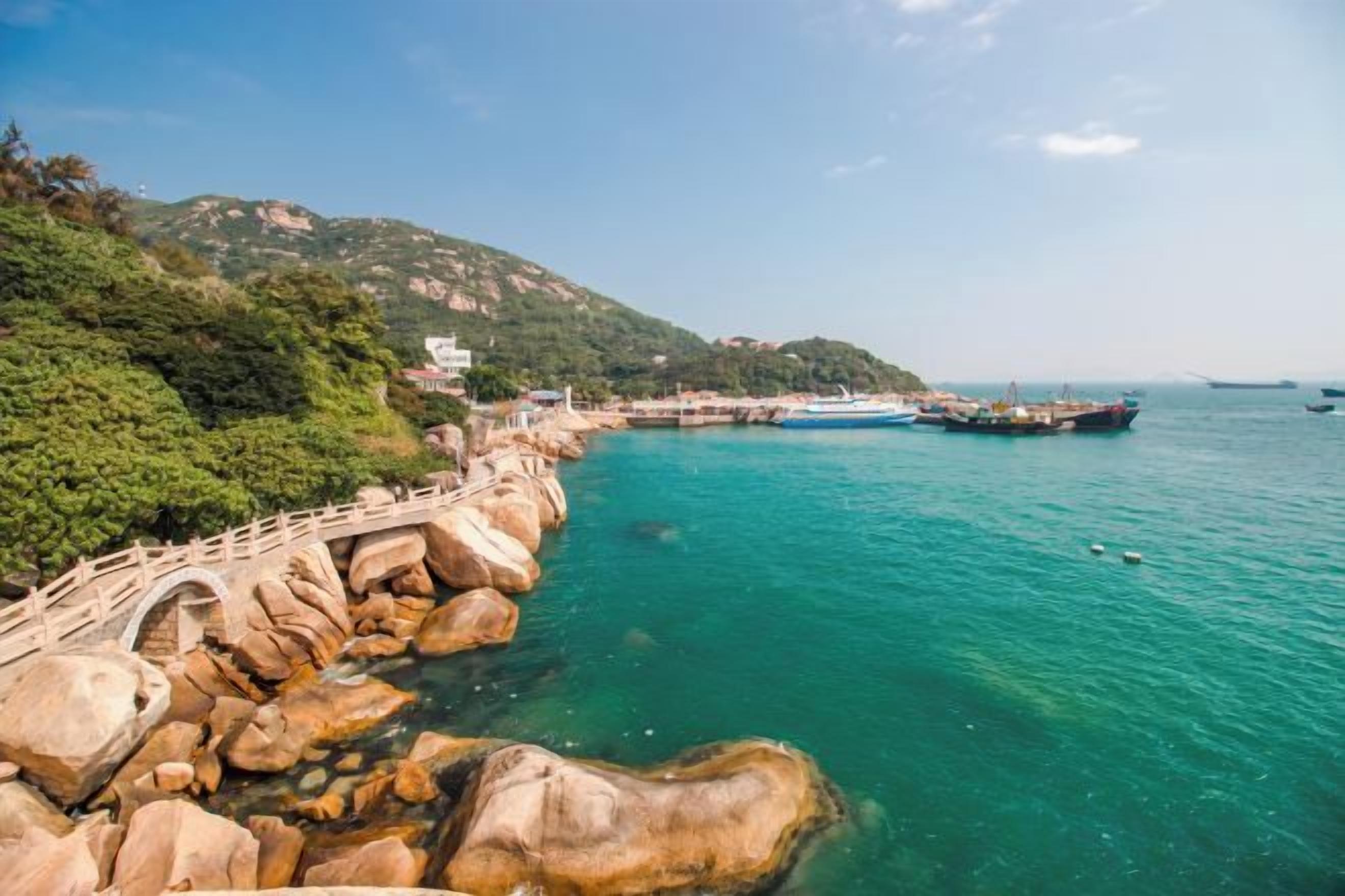 A coastal area with a rocky shoreline, a bridge, and boats in the water.