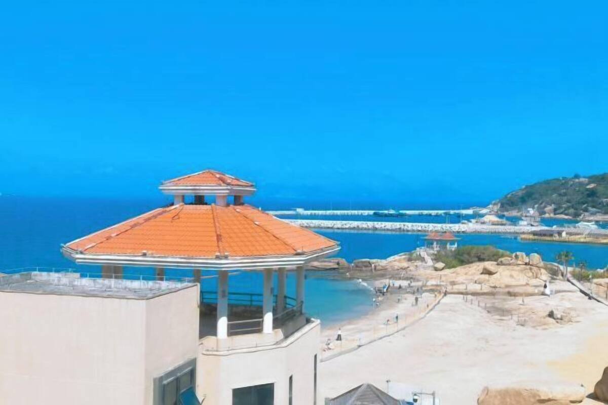 A coastal view with a gazebo, rocky beach, and a pier extending into the sea.