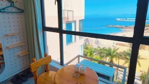 A room with a large window overlooking a beach, a round wooden table with two salt shakers, and a chair. - Zhuhai Wailingding Island Wanghaige (Beach Swimming Area) (Zhuhai)